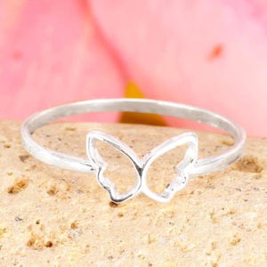 May include: A silver ring with a butterfly motif. The ring has a slender band and a butterfly-shaped centrepiece. The butterfly's wings are open, giving it an airy and elegant appearance. The ring is set against a neutral background.