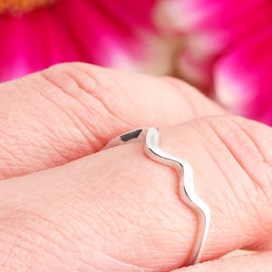 May include: A silver ring with a wavy design. The ring is on a person's finger.
