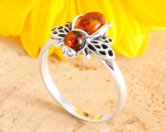 May include: A silver ring with a bee design featuring two amber stones. The bee is detailed with intricate wings and a textured body.