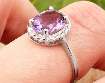 May include: A silver ring featuring a large, oval-cut amethyst gemstone. The purple gemstone is set in a decorative, openwork setting. The ring's band is a simple, polished silver.