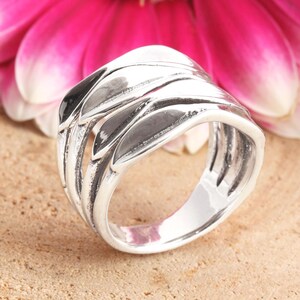May include: A silver ring with a wide band featuring a layered design of overlapping, curved shapes. The ring has a polished finish and a smooth, comfortable fit.