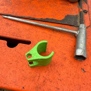 May include: A green plastic clamp and a silver wrench with a socket on a bright orange surface.