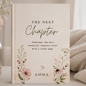 Puede incluir: Un libro de tapa dura de color crema con el texto THE NEXT Chapter y Sometimes the most beautiful chapters start with a blank page. La portada está decorada con ilustraciones de flores silvestres rosas y blancas y el nombre EMMA en negro.