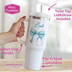 May include: White 40 oz. tumbler with a teal bow and stethoscope design. The tumbler has a comfort grip handle and includes a twist-top lid and straw. The tumbler is designed to fit in most cupholders. The name "Leah" is written on the tumbler.