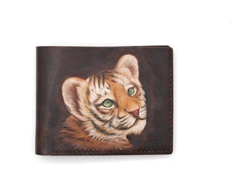 May include: A brown leather wallet with a detailed carving of a tiger cub with green eyes. The cub is looking to the right of the image.