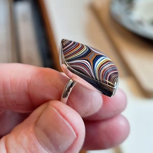 May include: A silver ring featuring a colourful agate stone set in a teardrop shape. The stone has a swirling pattern of brown, white, blue, and red.