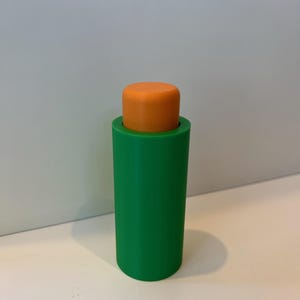 Pu&ograve; includere: Un tappo per bottiglia in plastica verde e arancione. Il tappo &egrave; cilindrico e ha una superficie liscia.