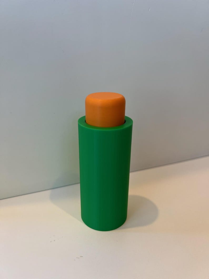 Pu&ograve; includere: Un tappo per bottiglia in plastica verde e arancione. Il tappo &egrave; cilindrico e ha una superficie liscia.