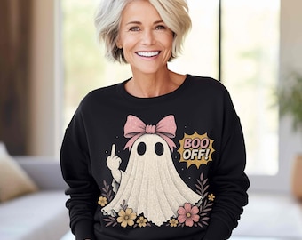 May include: A black long-sleeve sweatshirt featuring a graphic of a white ghost wearing a pink bow. The ghost is making a middle finger gesture. The text "BOO OFF!" appears in a yellow starburst shape, surrounded by small pink and yellow flowers.
