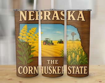 May include: A tumbler featuring a design with the word "NEBRASKA" at the top. The design includes illustrations of a field with tractors, yellow flowers, and corn, with the text "THE CORNHUSKER STATE".