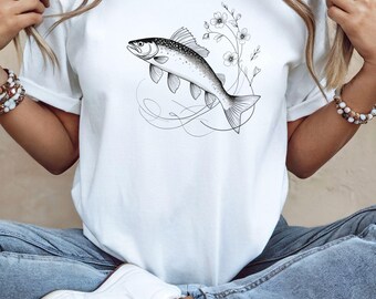 May include: White t-shirt featuring a detailed black and white illustration of a fish with floral accents. The design includes a fish swimming with delicate floral elements and swirling lines, creating an artistic and nature-inspired graphic.