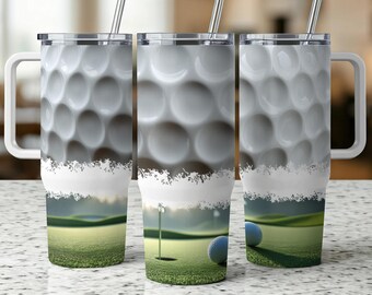 May include: Three stainless steel tumblers with golf ball patterns and handles. The design features a golf course scene with a green, a golf ball, and a flag. Each tumbler has a silver straw and a white handle.