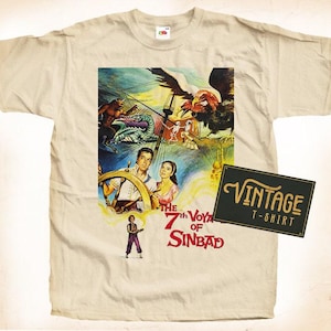 Peut inclure: Un t-shirt vintage avec une illustration colorée du 7ème Voyage de Sinbad. L'illustration comprend un navire, un oiseau géant et plusieurs personnages. Le texte "The 7th Voyage of Sinbad" est imprimé en rouge sur le t-shirt.