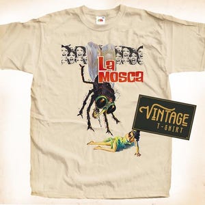 May include: A vintage beige t-shirt featuring a graphic of a large fly with the text "La Mosca" printed on it. The fly is depicted in a menacing way with large, red eyes. The t-shirt also features a vintage label that says "Vintage T-Shirt".