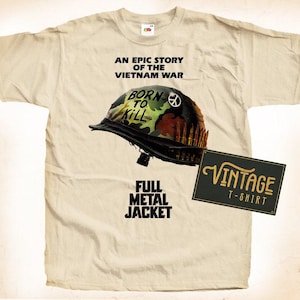 Può includere: Una t-shirt beige con un design vintage che presenta un elmetto militare con le parole "Born to Kill" su di esso. Il testo "Full Metal Jacket" è stampato sotto l'elmetto. Il testo "Vintage T-Shirt" è stampato su un rettangolo marrone.