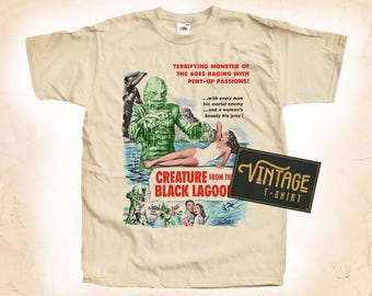 May include: A vintage t-shirt featuring a black and white illustration of a creature from the black lagoon. The creature is green and has a menacing expression. The text "Creature from the Black Lagoon" is printed in red and white. The t-shirt is beige and has a vintage look.