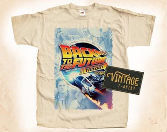 May include: A beige t-shirt with a vintage Back to the Future 30th Anniversary Trilogy design. The design features the DeLorean time machine, Marty McFly, Doc Brown, and the movie title.