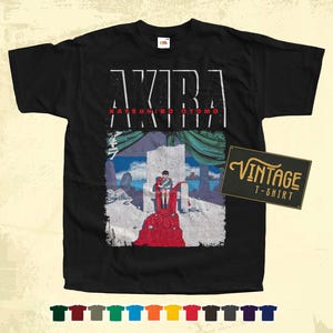 Może przedstawiać: Czarny vintage t-shirt z nadrukiem graficznym postaci z anime Akira. Na koszulce nadrukowany jest tekst "AKIRA" i "KATSUHIRO OTOMO".