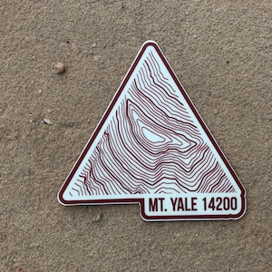 May include: A white triangular sticker with a brown outline and topographic lines. The sticker has the text "MT. YALE 14200" at the bottom.