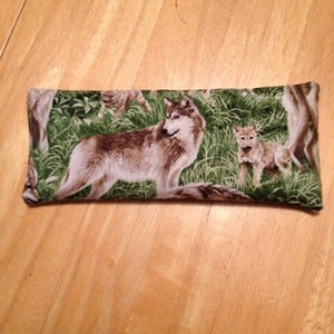 May include: A rectangular green and brown fabric pillow with a wolf and two wolf pups printed on it. The wolf is brown and gray with a white chest and the pups are brown and white.