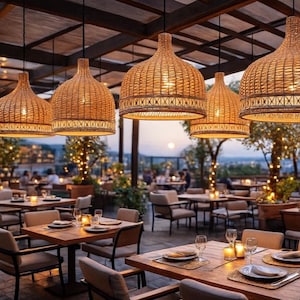 Könnte beinhalten: Eine Freiluft-Restaurantszene mit mehreren Tischen und Stühlen. Geflochtene Pendelleuchten hängen von der Decke. Die Tische sind mit Tellern, Gläsern und Kerzen gedeckt. Bäume und andere Pflanzen sind im Hintergrund zu sehen.