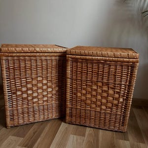 May include: Two natural woven wicker storage baskets with lids. The baskets are rectangular and have a light brown colour.