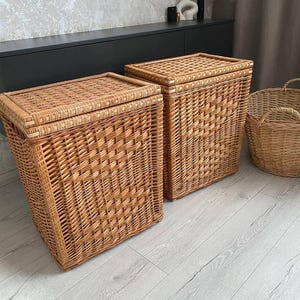 May include: Two rectangular, woven wicker laundry hampers with lids. The hampers are a light brown color and have a textured, basket-weave design. A round wicker basket with handles is also visible.