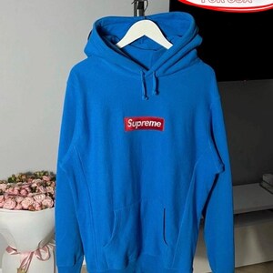 May include: Bright blue hoodie with a kangaroo pocket and a hood. The hoodie features a red and white Supreme logo on the chest. The text "FREE DUTIES FOR USA" is in a red oval in the background.