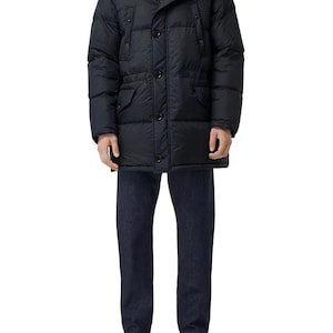 May include: A navy blue puffer jacket with a plaid-lined hood and button closure. The jacket has two front pockets and is worn with dark blue jeans and patterned trainers. The outfit is suitable for cold weather.