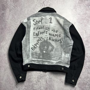 May include: Black denim jacket with a faded graphic on the back. The graphic includes the words "Step 1", "Establish the NAME", and "ENFANTS RICHES DÉPRIMÉS". The jacket has black sleeves and silver buttons.