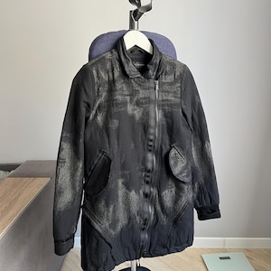 May include: A black zippered jacket with a silver-grey pattern. The jacket has two pockets on the front and a zipper closure.