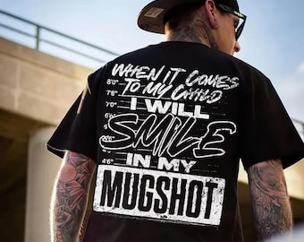 May include: Black t-shirt with white text that reads "WHEN IT COMES TO MY CHILD I WILL SMILE IN MY MUGSHOT." The shirt has a height chart on the left side. The person in the image is wearing a black cap and sunglasses.