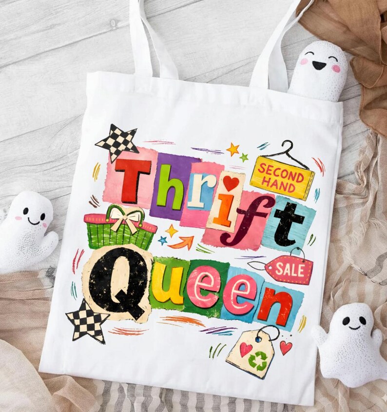 May include: White tote bag with the words "Thrift Queen" in colorful, block letters. The design includes a shopping basket, stars, hearts, and the words "Second Hand" and "Sale". Two small ghost-shaped plushies are visible.