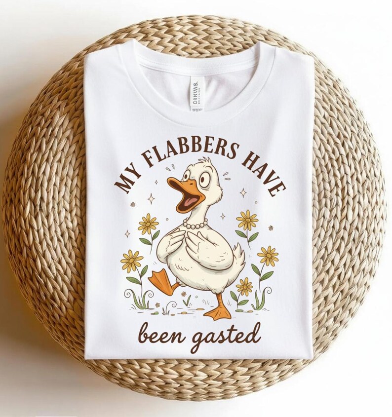 May include: White t-shirt with a cartoon duck graphic. The duck is wearing a pearl necklace and is surrounded by yellow flowers. Text on the shirt reads "MY FLABBERS HAVE been gasted."