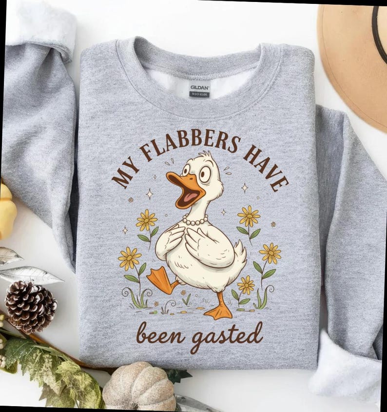 May include: A light gray sweatshirt featuring a cartoon duck with the text "MY FLABBERS HAVE been gasted". The duck is wearing a pearl necklace and surrounded by yellow flowers. The sweatshirt is a crew neck.