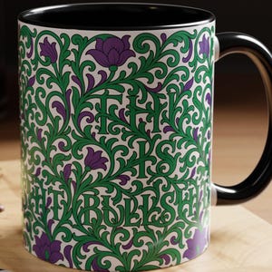 May include: A ceramic mug with a black interior and handle, featuring a white exterior decorated with a dense green vine and purple flower pattern. The text 'THIS IS BULLSHIT' is integrated into the intricate floral design in a dark green font.