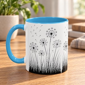 May include: A white ceramic mug with a bright blue handle and interior rim. The exterior features a black graphic print of dandelion seed heads and grass. The text "FUCK THIS SHIT" is printed vertically along the stems of two dandelions.