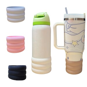 Puede incluir: Tres recipientes de bebidas aislados con mangas de silicona. Los recipientes son blancos con diferentes diseños. Un recipiente tiene una tapa verde y una manga de silicona blanca. Otro recipiente tiene una manga de silicona marrón y un diseño de dibujos animados. El tercer recipiente tiene una manga de silicona rosa.