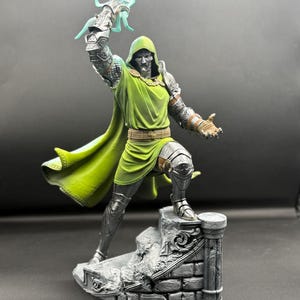 May include: A detailed figurine of a character wearing silver metallic armor and a green hooded tunic. The figure stands on a stone-textured base, holding a translucent light blue lightning bolt effect in one raised hand and reaching out.