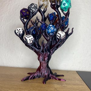 Peut inclure: Un arbre imprimé en 3D noir et violet avec des branches tenant divers dés colorés. Les dés sont de formes et de tailles différentes, y compris un d4, d6, d8, d10, d12 et d20.