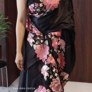 May include: Black fabric with embroidered pink floral design. The fabric is draped, showcasing the floral pattern. The text "TUS-PRS-150126" is visible on the fabric. The overall theme is clothing.