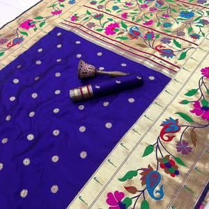 May include: A royal blue sari with gold floral border and accents. The sari features a detailed floral pattern in pink, green, and blue. The word "Parpal" is in the top left corner. A matching rolled fabric and decorative item are included.