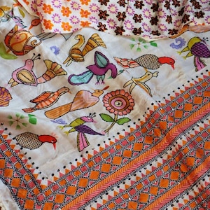 May include: A white textile with colorful embroidered birds and floral patterns. The design includes orange, pink, and purple accents, with a geometric border and the text "DBC".