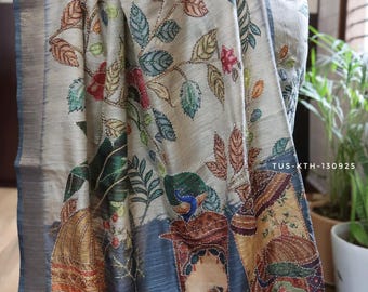May include: A beige saree featuring intricate hand-painted designs of colorful leaves, flowers, and a peacock. The lower border displays detailed illustrations of figures in traditional attire and architectural elements, accented with sequins. TUS-KTH-130925.