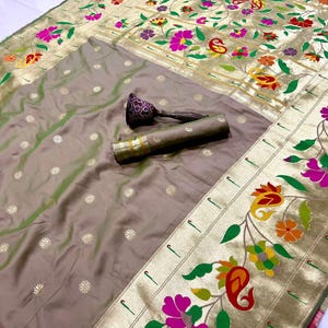 May include: A luxurious, intricately designed saree in shades of gray and gold. The fabric features a floral pattern with pink, green, and yellow accents. A rolled-up portion of the saree and a decorative item are visible.