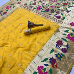 May include: A yellow silk saree with a gold border and floral design. The saree has a matching yellow blouse piece and a decorative item. The gold border features colorful flowers and paisley patterns.