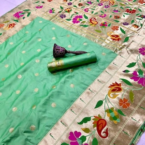 May include: A light green silk sari with gold floral embroidery and a decorative border. The sari features a rolled-up section and a decorative object with a dark purple handle.