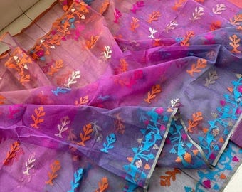 May include: A sheer, purple saree with intricate floral embroidery in orange, blue, and pink. The fabric transitions from a lighter pink to a deeper purple, with detailed borders. The saree is folded, showcasing its delicate texture and vibrant colors.