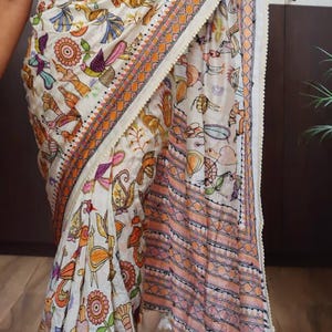 May include: White saree with a colorful bird and floral pattern. The saree has an orange and white border with a decorative trim. The text "DBC" and "KTH-LMB-15092" are visible on the saree.