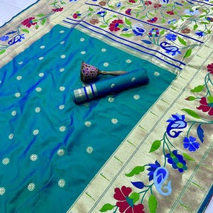 May include: A teal-colored sari with gold trim and floral embroidery in red, blue, and green. The fabric is folded and rolled, with a matching decorative piece. The sari features a detailed border design and small, gold-colored floral accents.